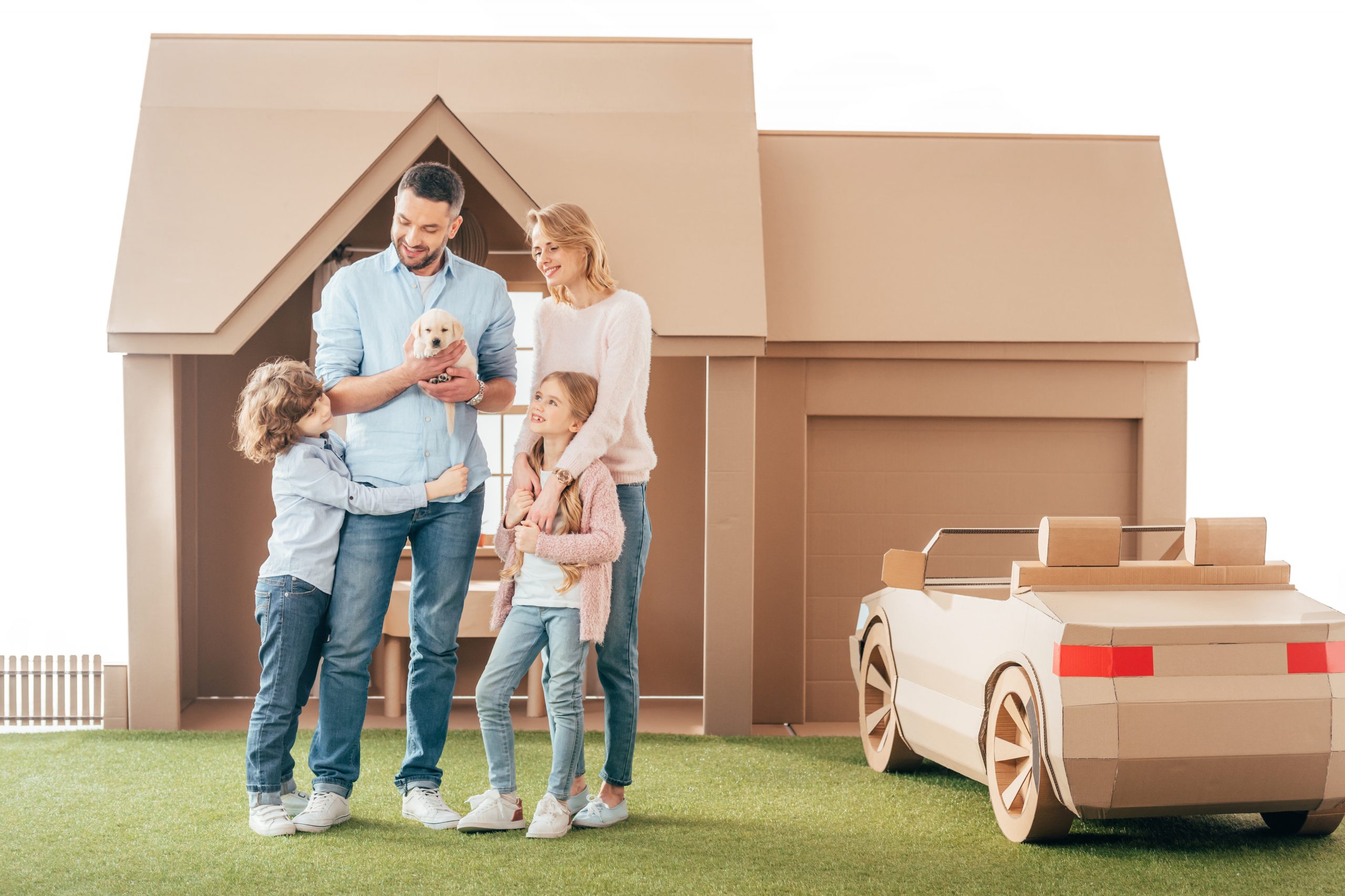 young family with adorable puppy on yard of cardboard house isolated on white